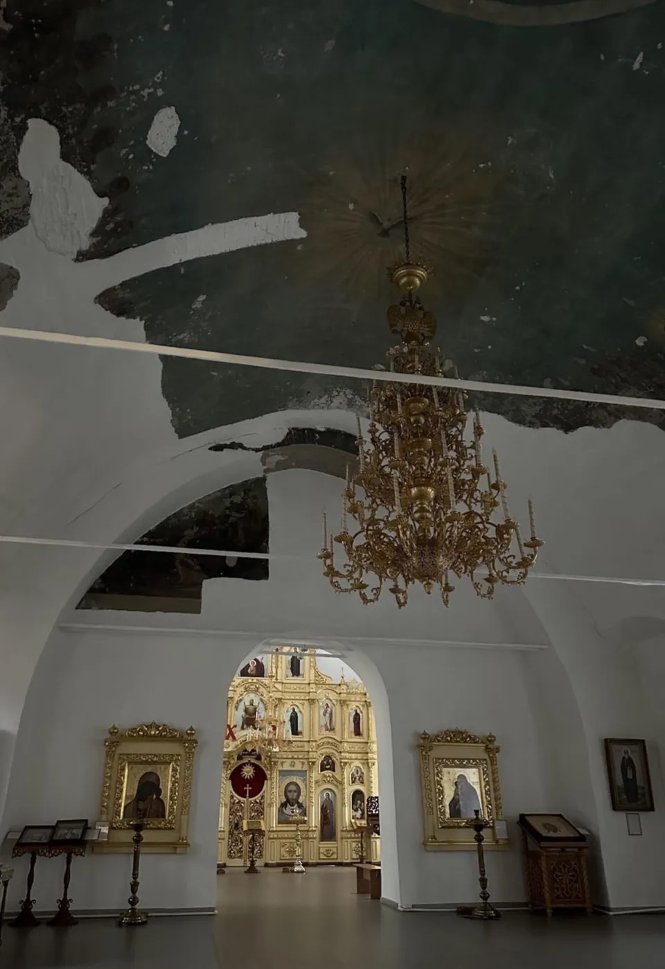 Повреждённый свод и потрескавшаяся штукатурка внутри Спасского храма, паникадило на фоне
